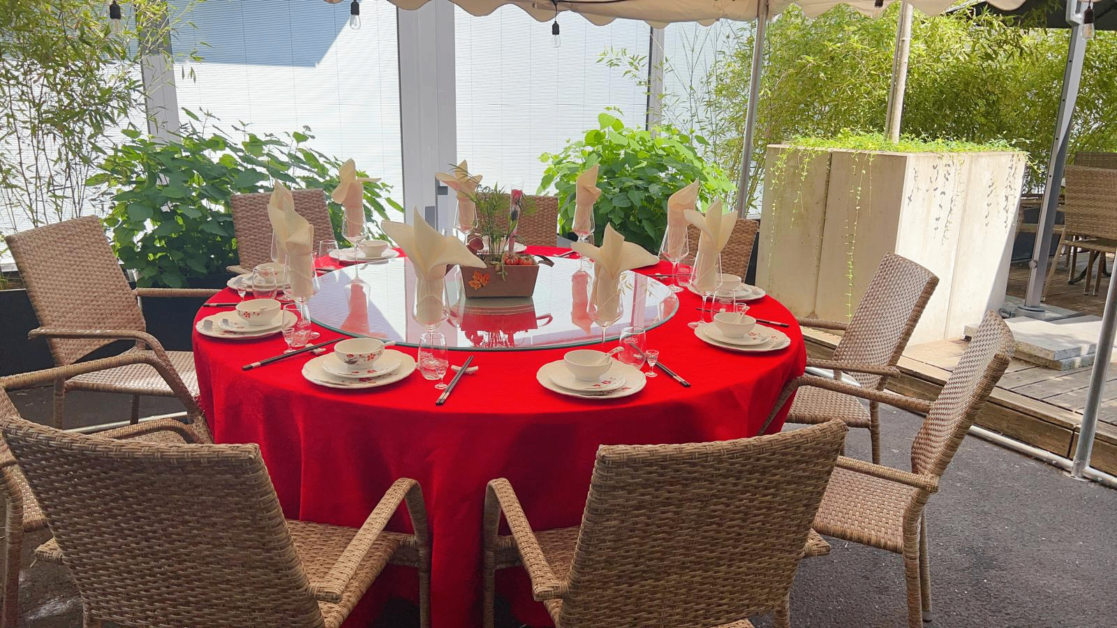 Runder Esstisch mit roter Tischdecke und Drehteller im begrünten Gartenpavillon