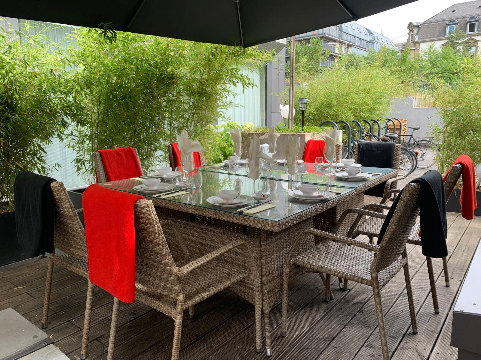 Terrasse mit langem Esstisch, roten Läufern und Bambus im Bahnhofsviertel