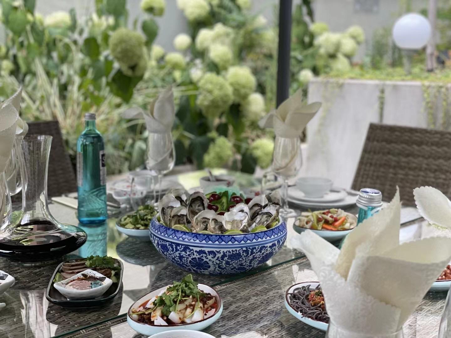Festlich gedeckter Gartentisch mit Austern in blau-weißer Porzellanschale und Sichuan-Vorspeisen